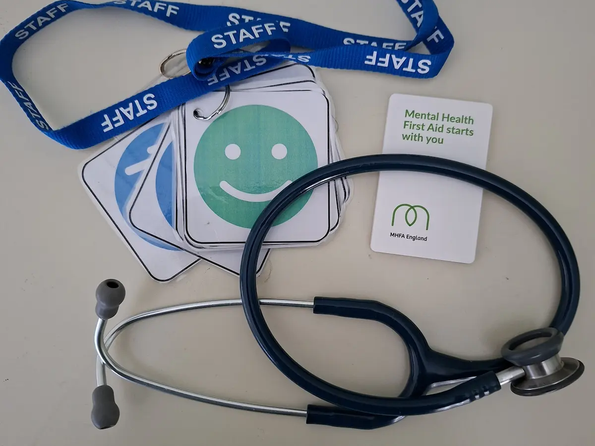 A stethoscope, staff lanyard and mental health first aid cards on a desk